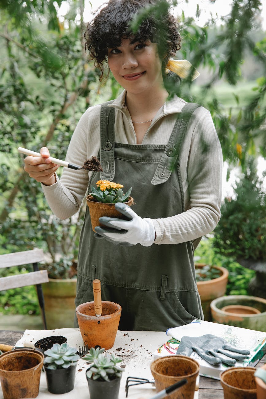 ethnic female gardener planting flower in pot