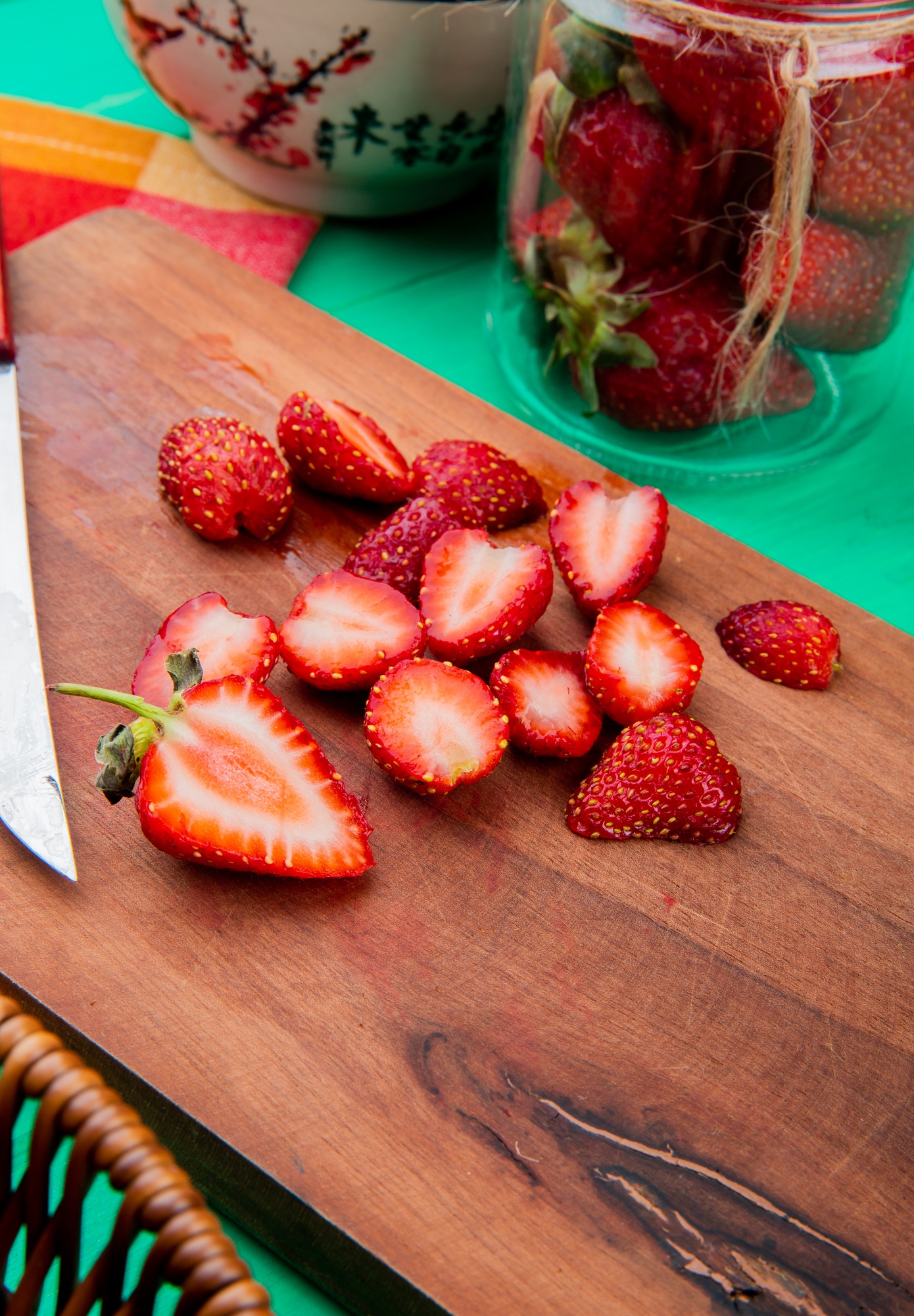 side view of cut strawberries on cutting board with bowl of strawberries on green background