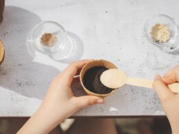 A caucasian girl plants seeds in a cardboard cup picking up the ground.