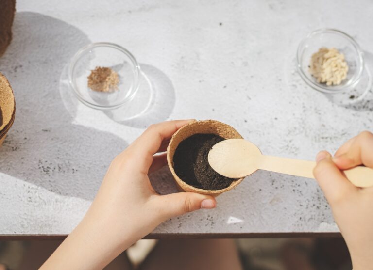 A caucasian girl plants seeds in a cardboard cup picking up the ground.