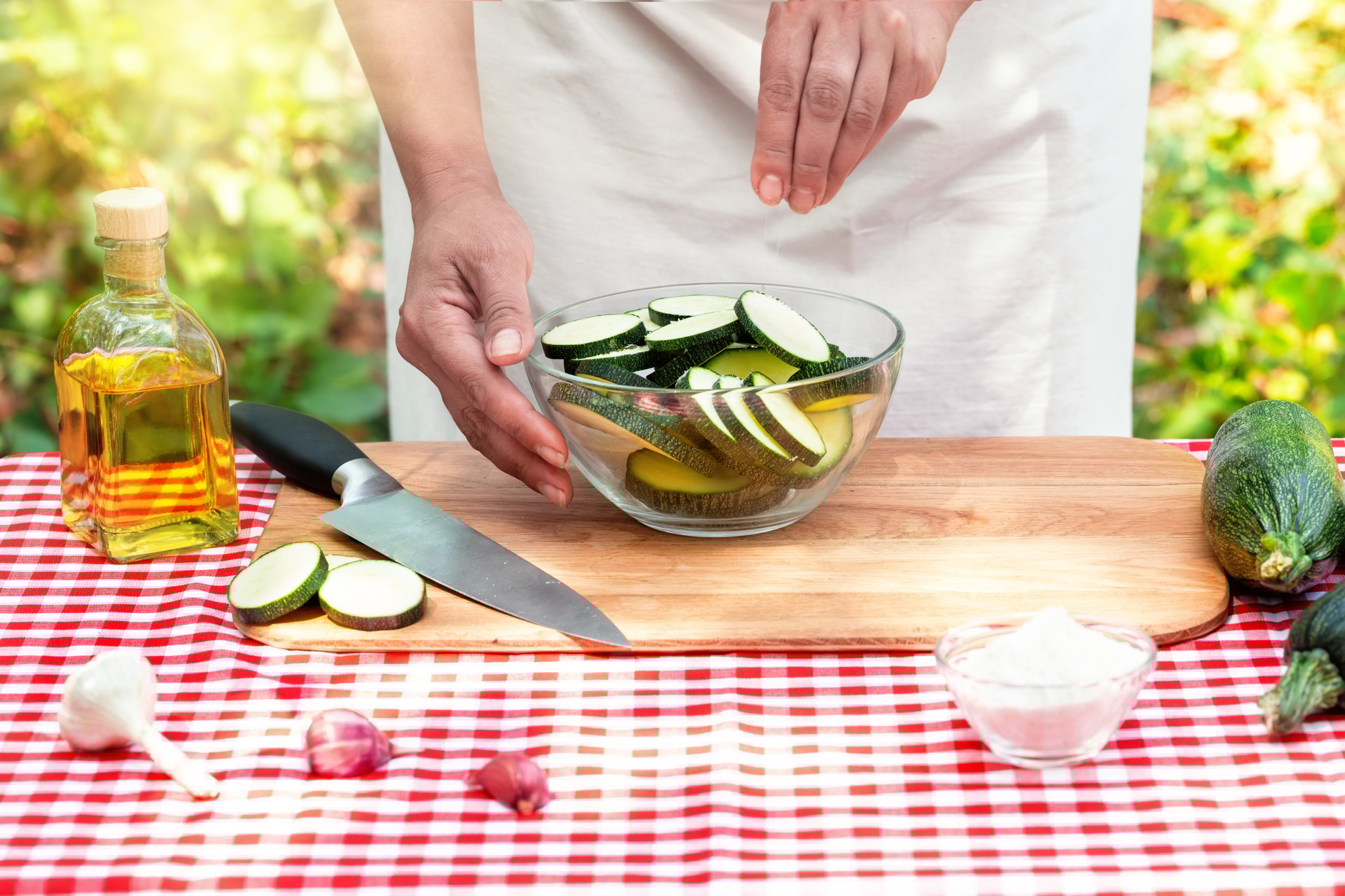 Female cook salt sliced zucchini in a transparent bowl
