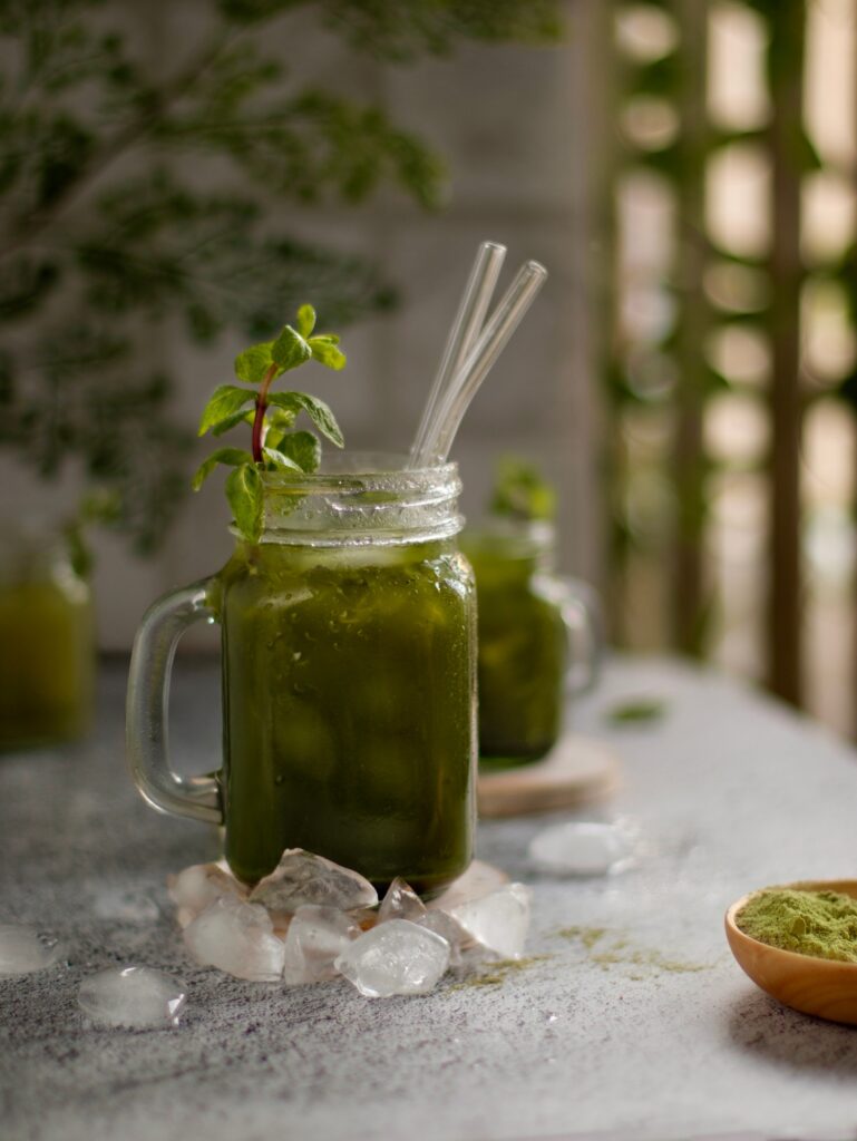 Natural background. Matcha ice tea with a mint in a glass, cocktail straws, on a wooden stand.