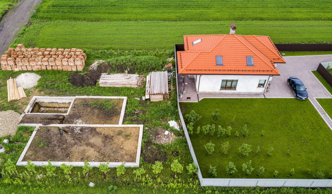 Aerial top view of a private house with attic windows on roof, paved yard with green grass lawn and