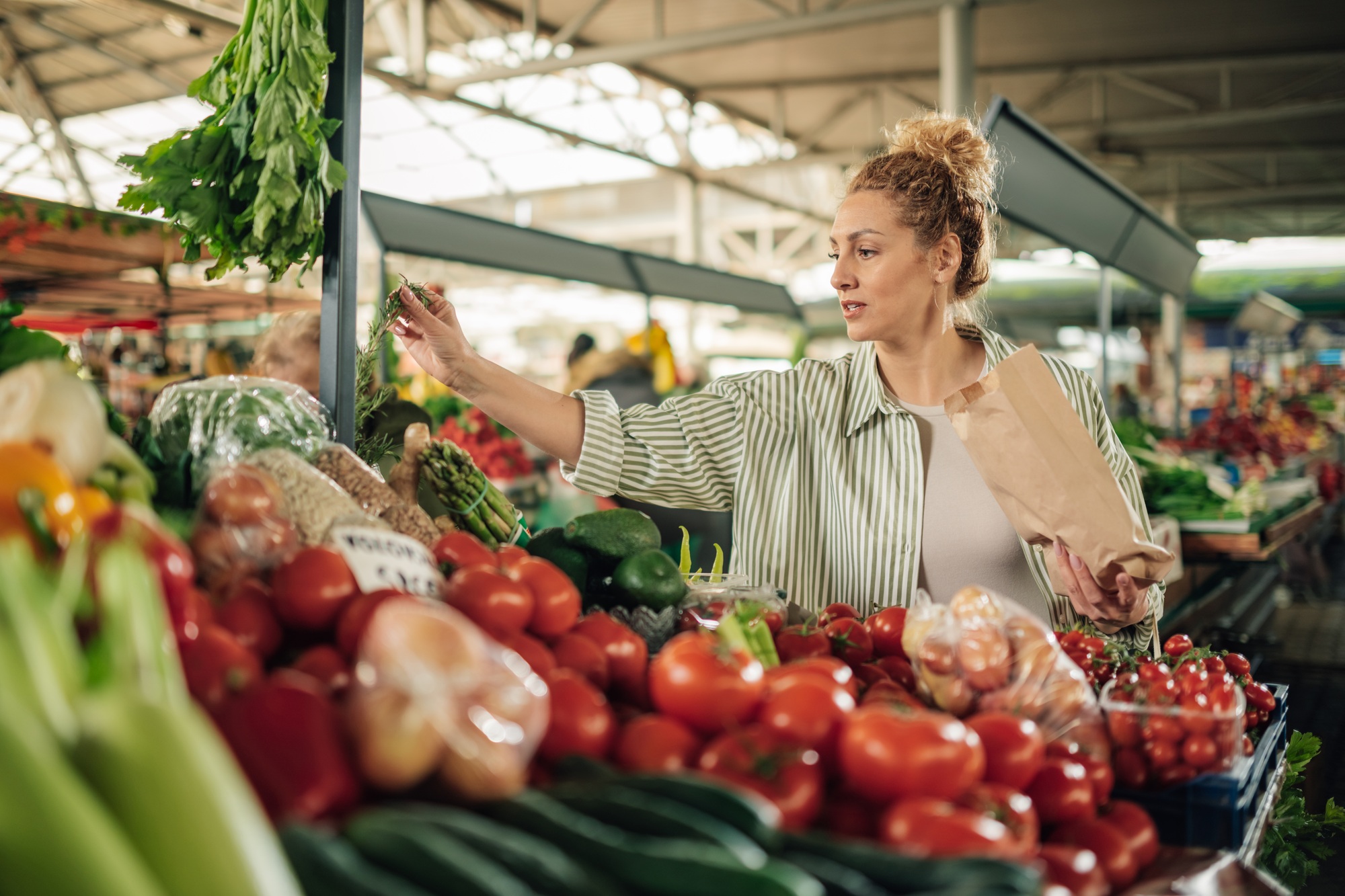 Shopper with paper shopping bag choosing vegetables at food market.