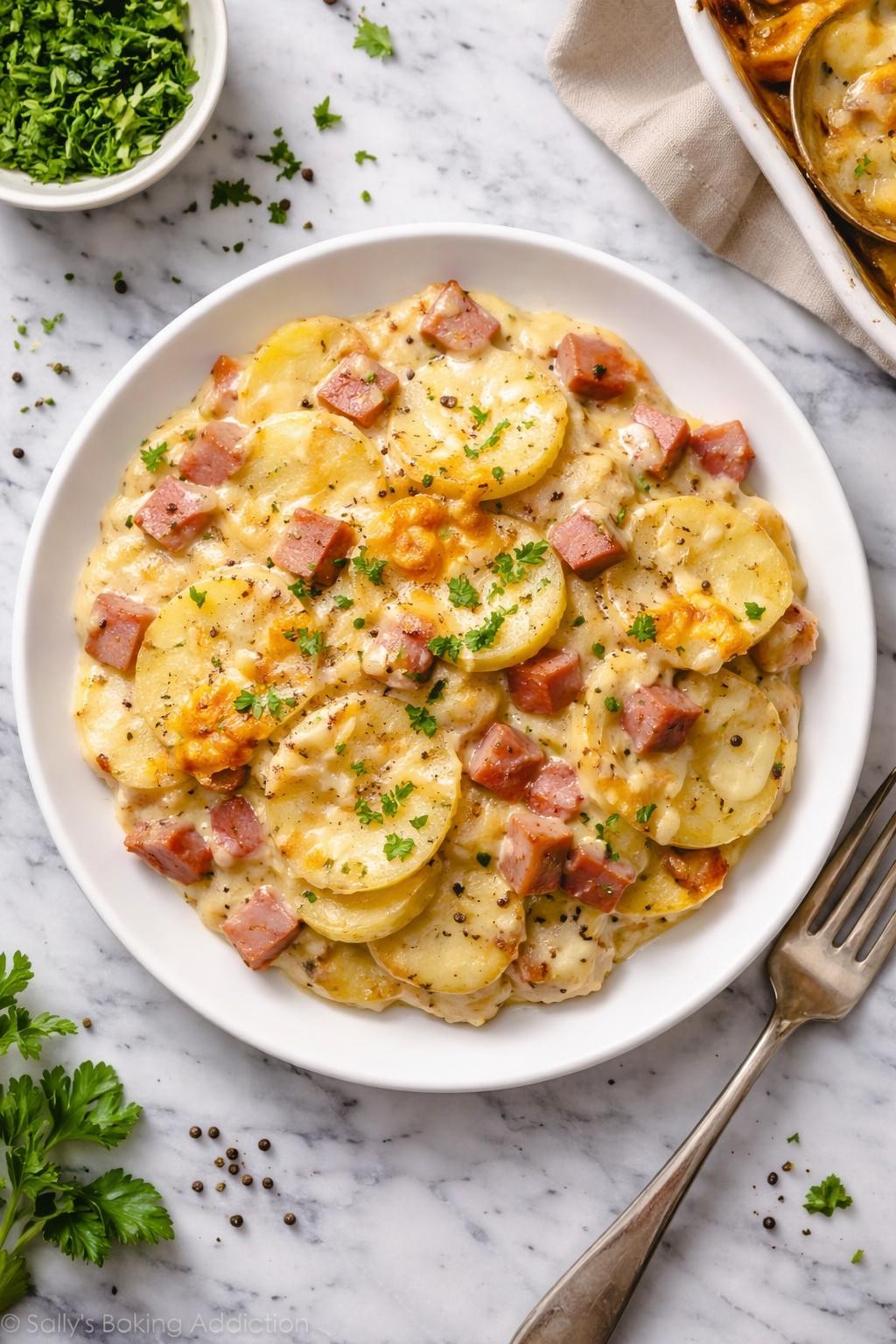 An overheard picture view of a plate of Scalloped Potatoes and Ham sitting on a marble countertop table in the kitchen, professional food photography style.