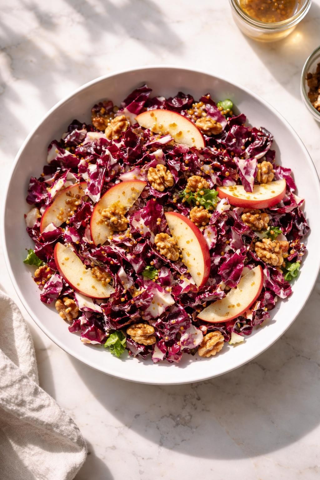 Image Prompt: Realistic top-down editorial food photography of a radicchio salad with walnuts in a shallow white bowl on a light marble countertop, chopped radicchio with toasted walnuts, apple slices, and glossy honey mustard dressing, bright natural daylight, soft shadows, clean editorial food styling, realistic textures, no people, no hands, no text, no watermarks, no props with writing.