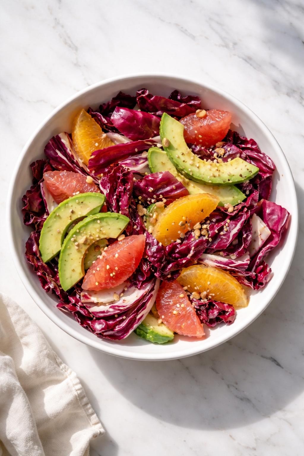 Image Prompt: Realistic top-down editorial food photography of a radicchio salad with avocado and citrus in a white bowl on a clean marble countertop, torn radicchio leaves with avocado slices, grapefruit segments, orange segments, and light citrus vinaigrette, bright natural light, soft shadows, clean composition, high detail, realistic food texture, no people, no hands, no text, no watermarks, no props with writing.