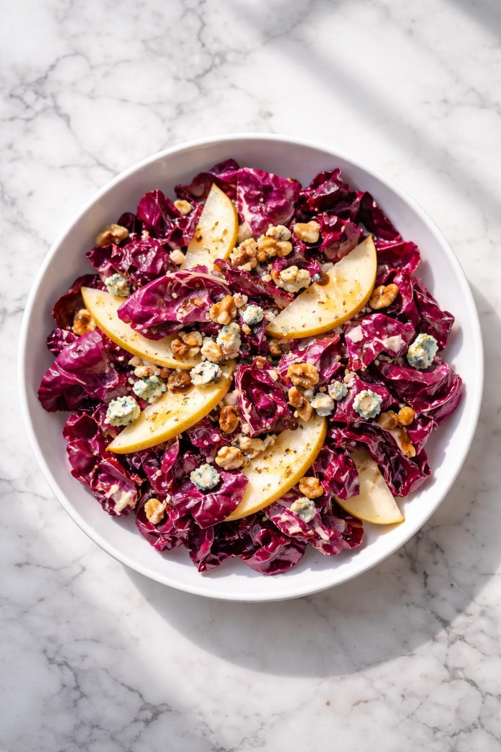Image Prompt: Realistic top-down editorial food photography of a radicchio salad in a wide white bowl on a clean white and gray marble countertop, chopped deep purple radicchio leaves with thin pear slices, blue cheese crumbles, chopped walnuts, and light balsamic dressing, bright natural window lighting, soft shadows, clean composition, high detail, realistic food texture, elegant homemade salad mood, no people, no hands, no text, no watermarks, no props with writing.