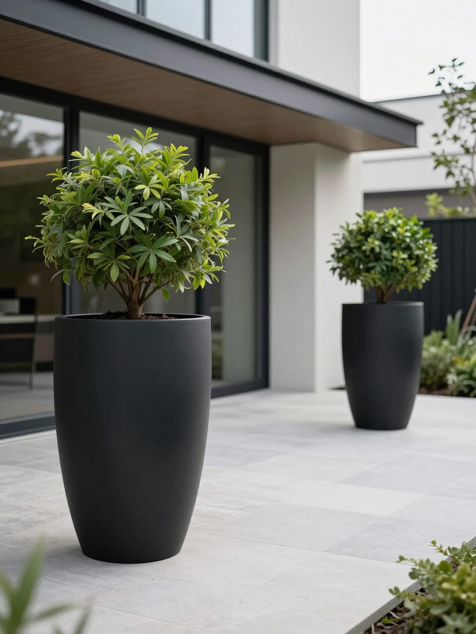 Image Prompt: A sleek modern patio with tall matte black garden planters, architectural plants, clean paving, minimalist home exterior, premium outdoor styling, crisp and elegant landscaping, soft daylight, realistic DSLR photo quality, no people, no watermarks on images.