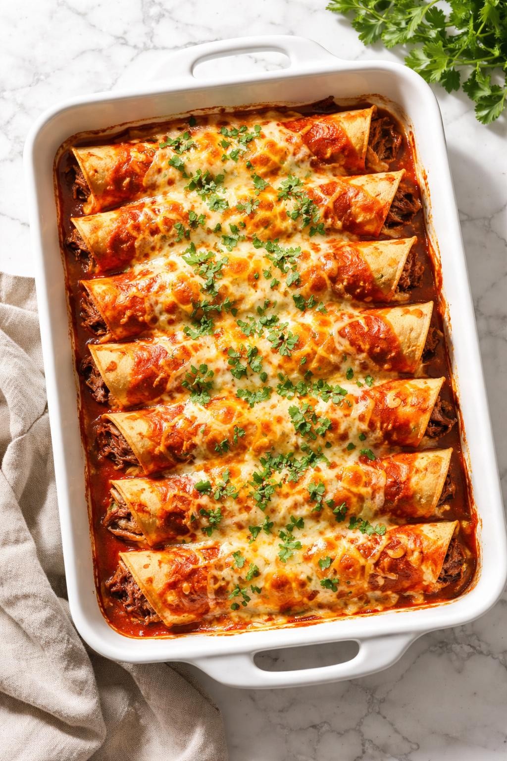Image Prompt: Realistic top-down editorial food photography of baked steak enchiladas in a casserole dish on a white marble countertop, corn tortillas rolled with shredded steak and covered in red enchilada sauce and melted cheese, topped with cilantro, bright natural daylight, soft shadows, cozy homemade dinner mood, high detail, realistic food texture, no people, no hands, no text, no watermarks, no props with writing.