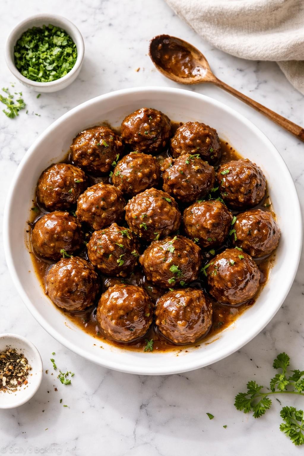 Image Prompt: Realistic top-down editorial food photography of onion soup mix meatballs on a clean white and gray marble countertop, browned homemade beef meatballs glazed in a savory sauce, served in a simple white dish with chopped parsley, cozy homemade appetizer or dinner styling, bright natural window lighting, soft shadows, clean composition, high detail, realistic food texture, no people, no hands, no text, no watermarks, no props with writing.