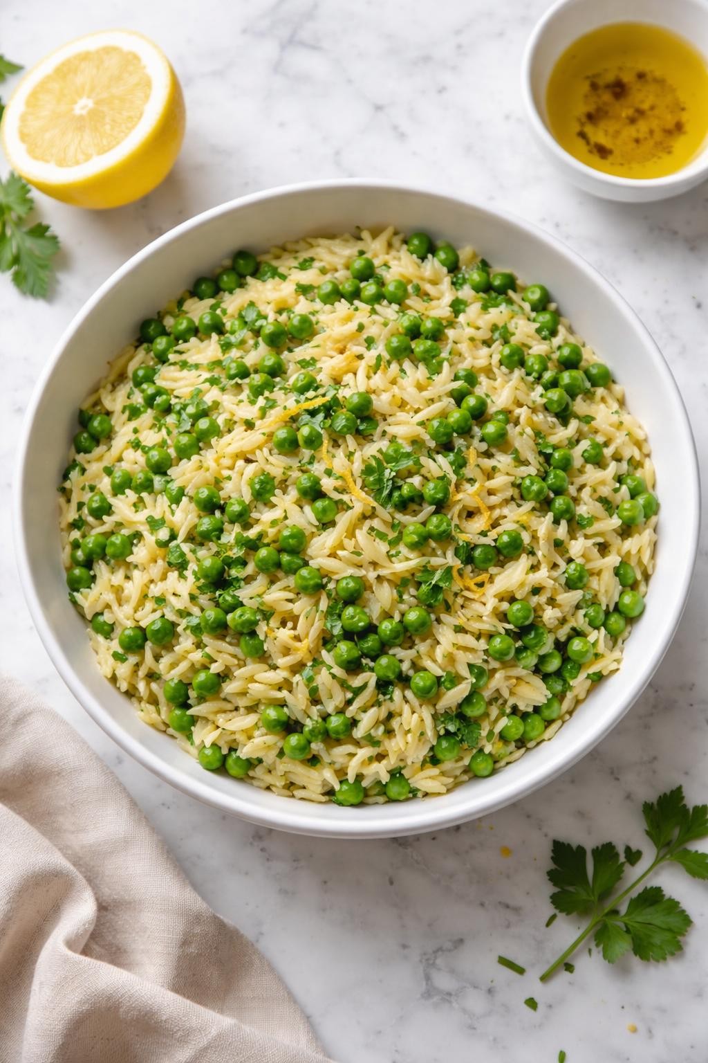 Image Prompt: Realistic top-down editorial food photography of a bowl of vegan lemon herb orzo with peas on a clean white and gray marble countertop, tender orzo mixed with green peas, parsley, lemon zest, and olive oil in a simple white bowl, bright fresh homemade meal mood, natural window lighting, soft shadows, clean composition, high detail, realistic food texture, no people, no hands, no text, no watermarks, no props with writing.
