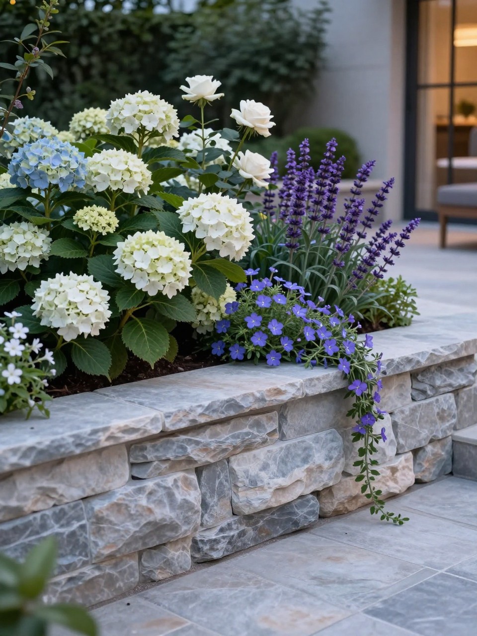 A stylish retaining wall flower bed near a patio with a broad low wall that feels like casual seating, smooth stone retaining wall, planted with hydrangeas, white roses, purple salvia, and trailing lobelia, elegant patio garden design, soft evening light, realistic outdoor living space, no people, no text, no watermarks on images.