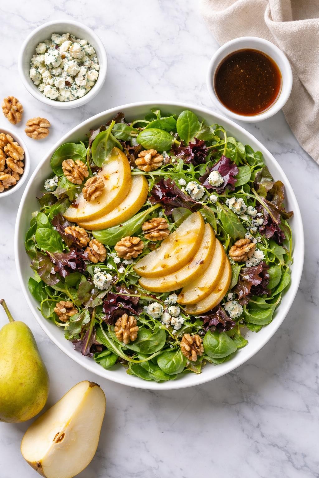 Image Prompt: Realistic top-down editorial food photography of a pear and blue cheese spring mix salad on a clean white and gray marble countertop, filled with spring mix greens, sliced pears, blue cheese crumbles, walnuts, and balsamic vinaigrette, elegant everyday homemade salad styling, soft natural daylight, clean composition, high detail, realistic food texture, no people, no hands, no text, no watermarks, no props with writing.