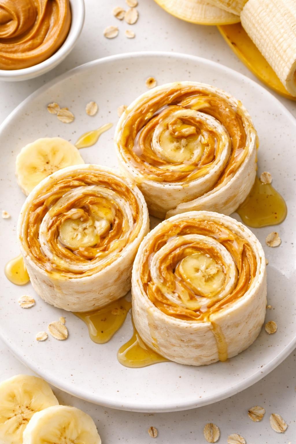 "Top-down realistic shot of three flour tortilla roll-ups cut into pinwheels, showing a swirl of peanut butter and mashed banana inside. A small drizzle of honey on top. Bright natural light, no-cook kid-friendly lunch, no people, no hands, no text, no watermarks."