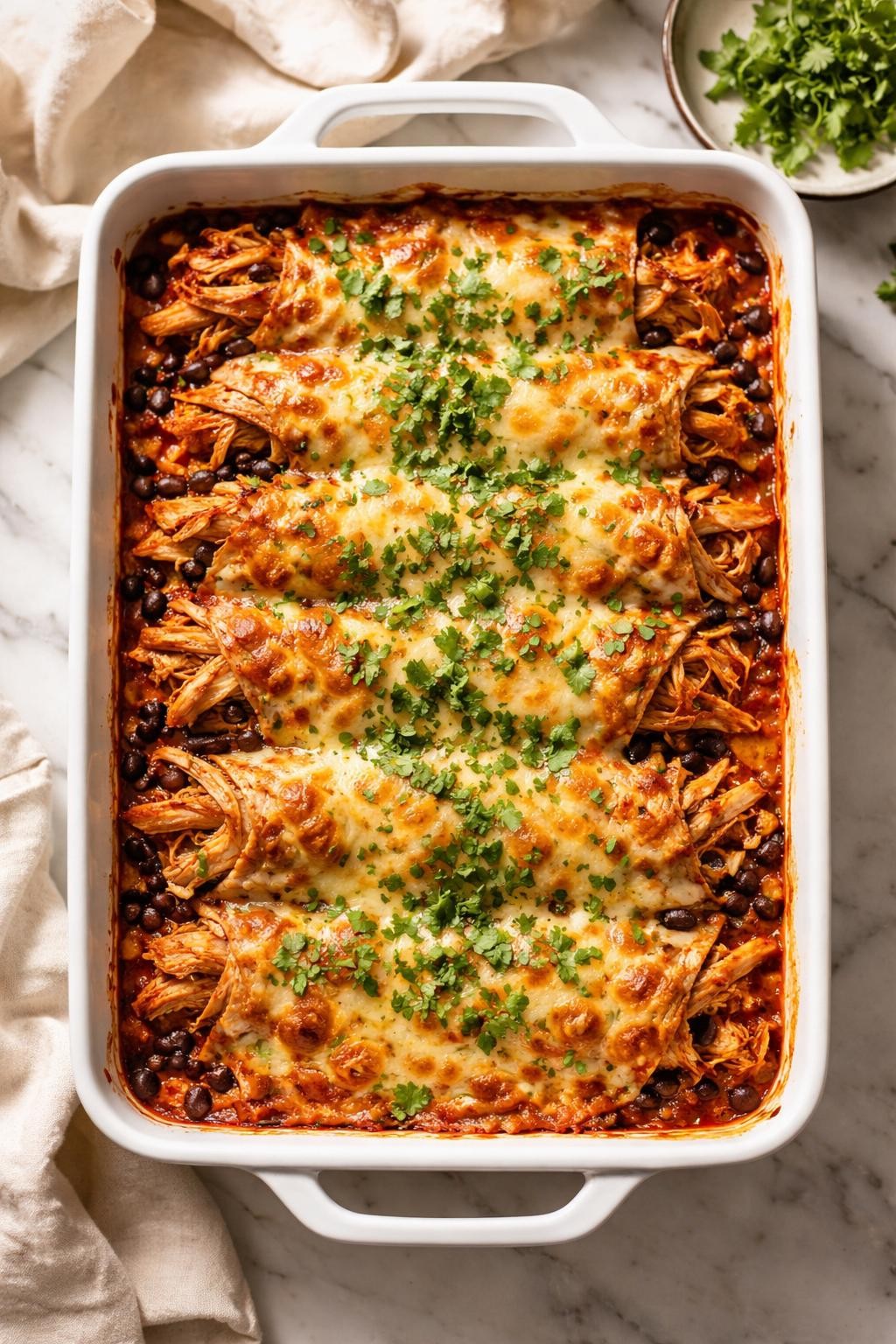 Image Prompt: Realistic top-down editorial food photography of a high protein Mexican chicken enchilada bake in a baking dish on a clean marble countertop, layers of shredded chicken, enchilada sauce, black beans, tortillas, and melted cheese, chopped cilantro on top, warm natural light, cozy homemade dinner mood, no people, no hands, no text, no watermarks, no props with writing.