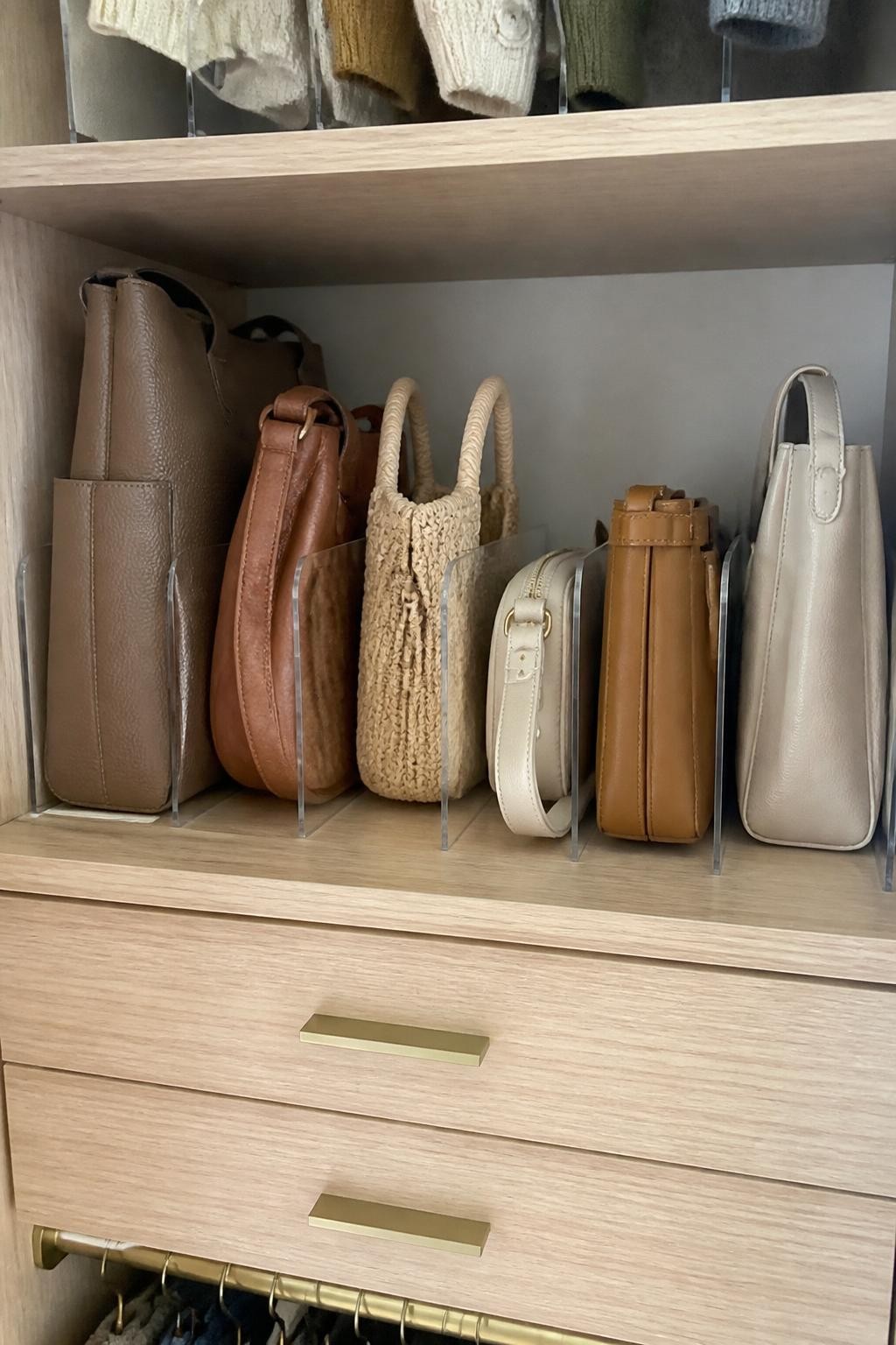 Image prompt: Closet shelf showing six handbags stored upright like books between simple acrylic dividers, including a structured tote, soft shoulder bag, woven summer bag, small crossbody, and neutral work bag, each lightly stuffed to hold its shape, photographed in natural iPhone photo quality, warm daylight, realistic leather and fabric textures, calm residential bedroom closet, slightly varied bag sizes, no luxury logos, no people, no watermarks on images.