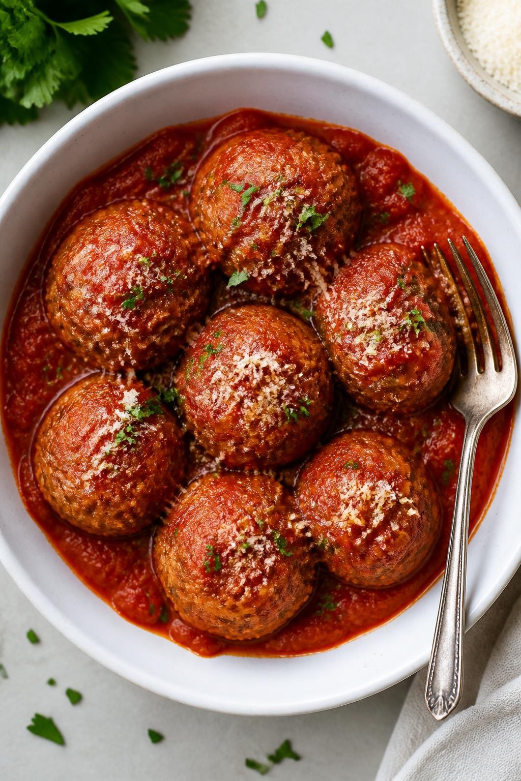 Photo prompt: Realistic top-down editorial food photography of a white bowl filled with six round turkey meatballs covered in red marinara sauce. A sprinkle of fresh parsley and grated Parmesan on top. The meatballs are slightly textured and moist. A fork rests on the side. Bright natural light, simple freezer-friendly dinner mood, no people, no hands, no text, no watermarks, no props with writing.